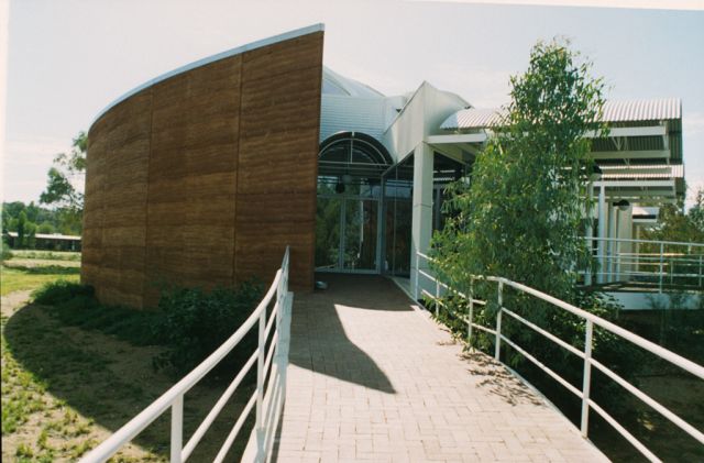 10m high walls, 300mm thick. One storey is underground in this picture. It was a 10m tall, curved, freestanding wall when it was first built, cantilevering off a basement concrete slab. Ramtec consulted and manufactured the rammed earth formwork for the job, gave training in rammed earth construction methodology, located the local red earthen materials, tested the materials locally in Central Australia and in Perth, approved and certified the materials and the wall strength, advised, tested, trialled and perfected the local mixing system for the rammed earth, supervised the construction of test walls, supervised the construction of full height walls, assisted the Architect (not Ramtec), advised and encouraged the local Structural Engineer (not Ramtec), who had learned on previous Ramtec 2 storey load bearing rammed earth walls with 300mm thick red rammed earth walls in Western Australia.